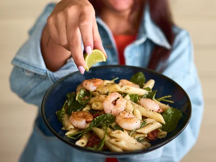 Eine lächelnde Frau hält die Pasta Prawn Wasabi auf einem Teller in die Kamera.