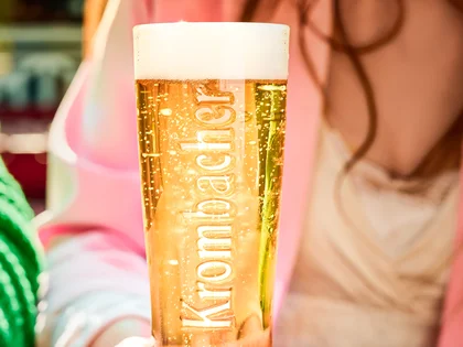 Eine Frau hält ein frisch gezapftes Krombacher Pils in der Hand. 