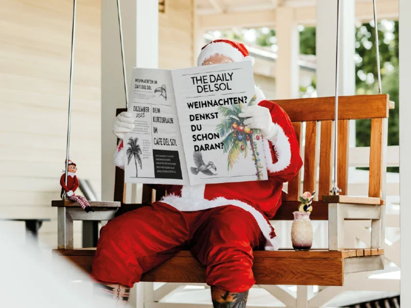 Ein Weihnachtsmann auf der Cafe Del Sol Schaukel liest Zeitung