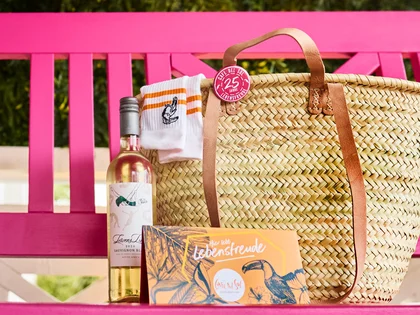 Eine Strandtasche mit Gutschein und Wein stehen auf der pinken Schaukel vom Cafe Del Sol 
