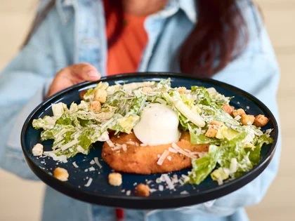 Eine lächelnde Frau hält das Chicken Caesar Schnitzel auf einem Teller in die Kamera.