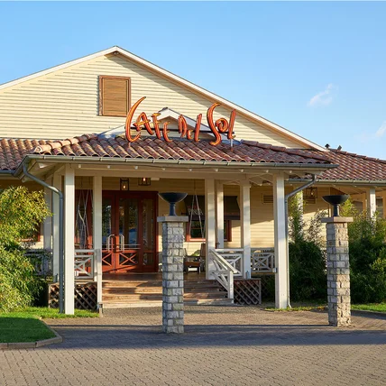 Holzgebäude im Landhausstil mit Veranda und Ziegeldach; Eingang mit Säulen, Treppe und dekorativen Außenlampen
