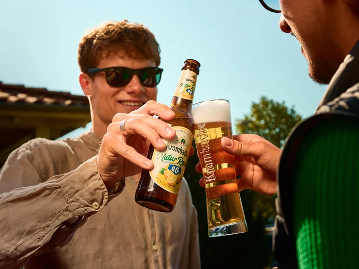 zwei Freunde stoßen an mit einem frisch gezapften Krombacher und einem Krombacher Natur Radler. 