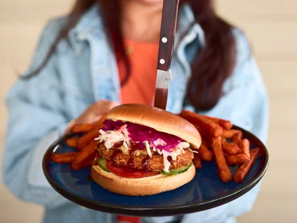 Eine lächelnde Frau hält den Maui Wowie Chicken Burger auf einem Teller in die Kamera.