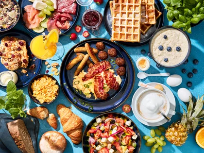 Draufsicht vom Frühstücksbuffet mit vielen Speisen auf blauen Untergrund.