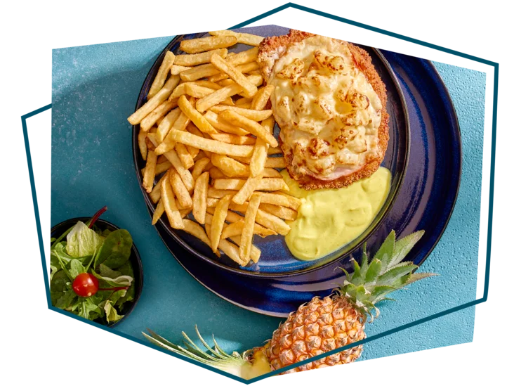 Draufsicht auf ein Schnitzel Hawaii auf einem Teller mit Beilagen drum herum.